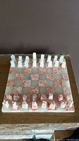 Full view of chessboard with all chess pieces arranged for play, showing pink and white onyx squares and carved pieces in two colors.