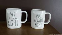 Front view of two white ceramic mugs labeled 'MR. RIGHT' and 'MRS. ALWAYS RIGHT' with handles, placed side by side against dark background.