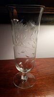 Full view of clear glass footed vase with sunflower and leaf etching, showing overall shape and design.