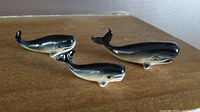 Three miniature whale figurines displayed on surface showing different views and relative sizes