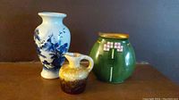 Photo showing all three items: a white and blue ceramic vase, a brown drip glaze ceramic vase, and a green pottery jug with floral design