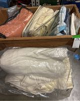 Various bed linens, pillow sack, and neck pillow packed together in a wooden crate.