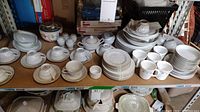 Full view of the china set displayed on a shelf, showing plates, cups, bowls, sugar bowls, creamers and saucers.