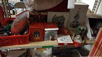Photo showing a shelf with assorted red basket containing Christmas bulbs, boxed ornaments, and village decoration boxes.