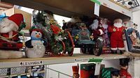 Wide view of shelf with multiple Christmas figures and decor including Santa figures, snowmen, and decorative sleigh.