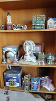 Photo of three shelves containing Christmas village miniature buildings, a white Ferris wheel decoration, miniature figures of people and a vintage car, and other small decor items.