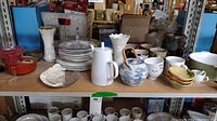 Wide view of mixed kitchenware items on shelf including mugs, vases, teapot, plates, and bowls.