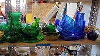 Shelf displaying various green glass vases, a green glass cruet bottle with stopper, a green plate and serving bowl, alongside blue glass nested bowls and vases.