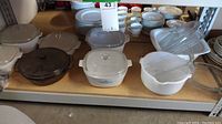 Shelf with various CorningWare and VisionWare baking dishes and lids, white opaque with blue pattern and solid white, plus one brown round VisionWare dish.