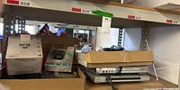 Shelf view of Canon DC10 box, Logitech mouse box, Avaya phone, and DVD players inside cardboard boxes