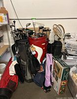 Overview showing three golf bags filled with clubs, boxed putting practice kit and badminton rackets nearby.