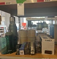 Shelf with Stanley thermos, travel bottle, masking tape rolls, staplers, mailing tape, and boxed Timex alarm clock