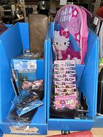 Photo showing a Hello Kitty toddler backpack, men's leather wallet, hair clips, and other small boxed toys arranged in blue cardboard display holders.