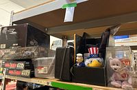 Shelf showing boxed Star Trek model set on top, Star Wars Monopoly games below, and assorted plush toys including TY Beanie bear on right