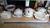 Shelf with tureens, covered baking dishes, bowls and colander insert arranged side by side.