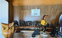 Group photo showing carved myrtlewood owl, resin elephant set on a wooden bridge, and Doberman figurines arranged on a shelf