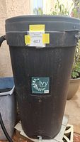 Tall black plastic rain barrel with a yellow auction sticker and an Ivy brand label on the front.
