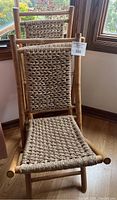 Front view of one bamboo folding chair with rope woven seat and back resting on wood floor near window