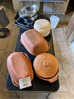 Overview of the clay roasting pots, microwave dishes and metal pans arranged on a table.