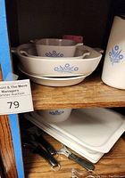 Photo showing nested square, rectangular, and oval Corning Ware dishes with blue cornflower design on a wooden shelf.