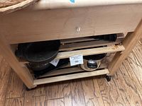 View showing lower shelf and casters of wood kitchen island, with measuring size tag