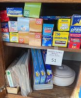 Shelf of various brands and types of kitchen wraps and bags including wax paper, parchment paper, plastic wrap, foil, slow cooker liners, and fold top bags