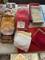 Top-down image of folded assorted kitchen towels with various patterns and colors including coffee cup and owl designs alongside a red cutting board.