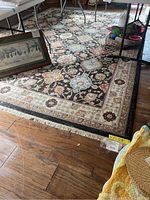 Full view of the large rectangular area rug with floral patterns and fringe at one end placed on wood floor under furniture.