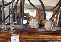 Full view of mantel clock and two glass taper candlesticks with purple candles on wooden surface with mirror reflection.