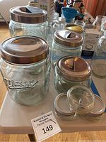 Wide view of six Mason jars and canisters with metal lids arranged on a white surface showing different sizes and sliding metal lids.