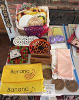 Various items arranged on a table including crochet trivets, metal trivets, linen napkins, wooden coasters, napkin holder, and banana bags