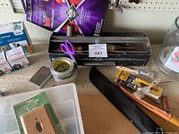 Various tools, old toolbox, machete in sheath, paint brushes, tapes, scissors, and hardware on a workbench