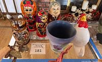 Photo showing entire lot including two Russian nesting dolls, Boris doll, wooden cat nesting set, hand-painted purple flower ceramic planter pot, and white chicken wall hook on display table.