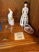 Photo showing all items: two crystal Tinkerbell figurines, ceramic bunny candle holder, ceramic napkin lady, and abalone shells arranged on a wooden shelf.
