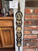 Full view of the 6 brass Royal Horse Guards badges mounted vertically on a black leather strap showing the overall arrangement and mounting.