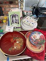 Photo showing several serving trays, paper plates, bowls, utensils, and Christmas themed items arranged on a table.