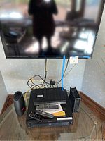 Vizio 40-inch flat screen TV on stand with connected devices below including Sony DVD player, VHS recorder, and multiple remotes.