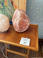 Photo showing two Himalayan salt lamps on wooden teak TV tray with watercolor peacock painting behind.