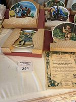 Eight Wizard of Oz collectible china plates from Edwin M Knowles with certificate of authenticity on cloth-covered display. Plates are partially boxed with distinct artwork of characters and scenes from the film.