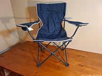 Front view of a blue fabric camping chair with foldable metal frame, armrests, and cup holder.