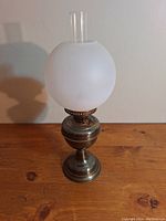 Front view of the antique brass oil lamp showing the frosted glass globe and brass body.