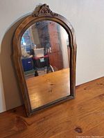Front view of antique wood framed wall mirror showing carved crest and arched top.