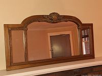 Front view of large rectangular wall mirror with wooden frame and ornate carved top center.
