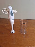 Photo of a white hand blender with two control buttons and clear plastic measuring cup with volume markings
