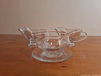 Two glass gravy boats and the glass serving bowl with plate and spoon set on the table