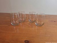 Four clear rounded glass tumblers on a wooden surface, showing side and top profile.