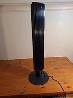 Tall black oscillating tower fan with vertical grill on wooden surface, showing full height and base