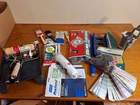 Photo showing various paint brushes, rollers, paint edger, paint tray, sanding abrasives, and Behr paint sample strips arranged on a wooden table.