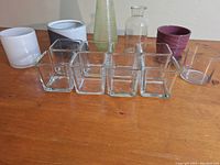 View of eleven planters, pots, and vases arranged in two rows on a wooden surface.