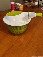 Full view of the salad spinner assembled, showing the clear bowl with green basket and white lid with green pull-cord handle.